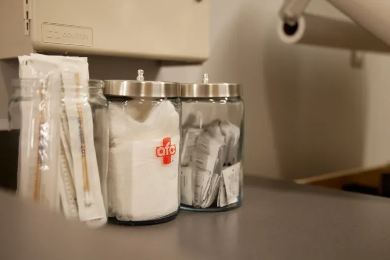 Medical supplies including packaged tongue depressors, gauze, and alcohol prep pads in jars neatly organized on a countertop at the medical center.