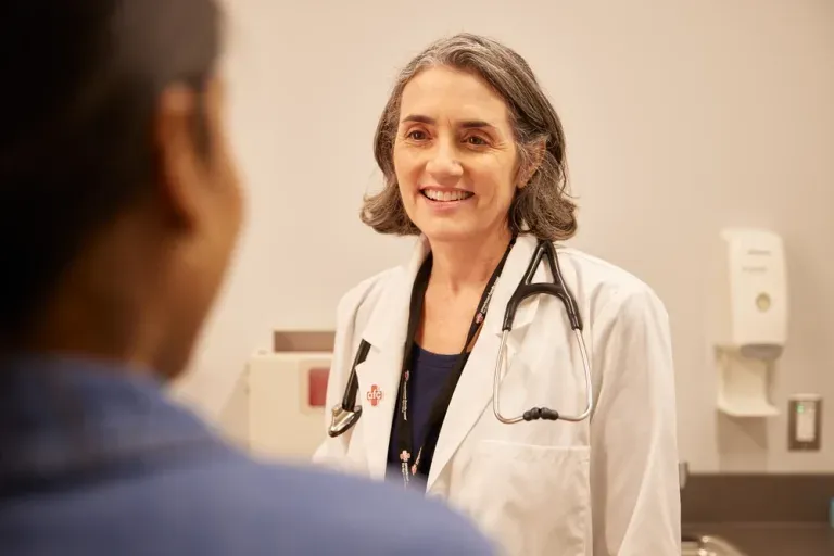 A female doctor with a stethoscope around her neck smiles while speaking to a patient in a walk-in clinic.