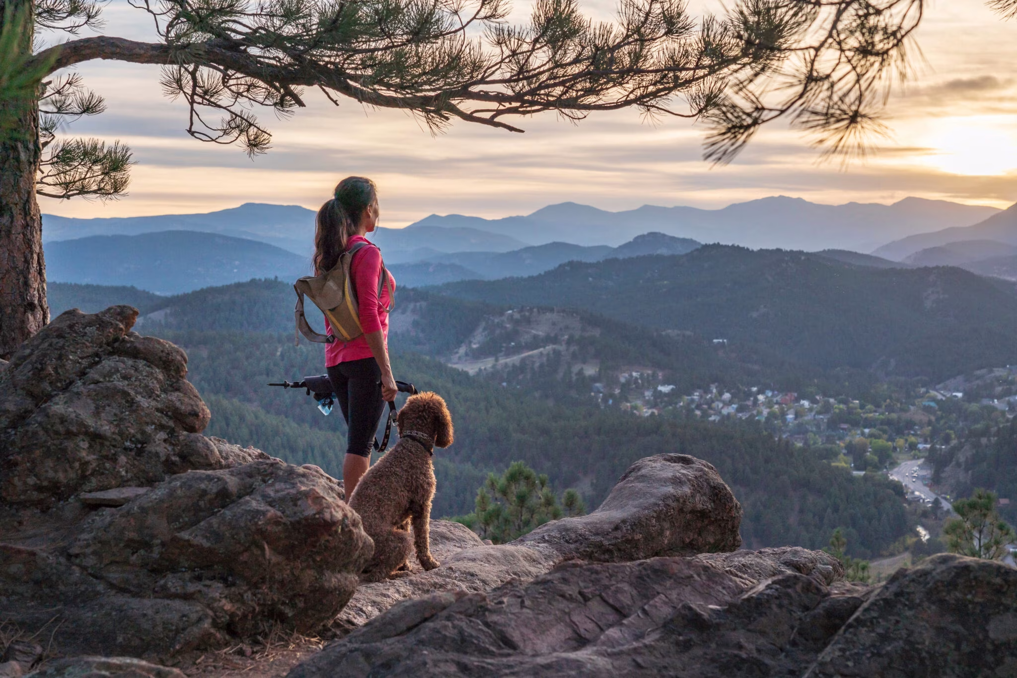 A hispanic woman is hiking with a dog, at sunset, in the Rocky Mountains near Denver, Colorado, USA