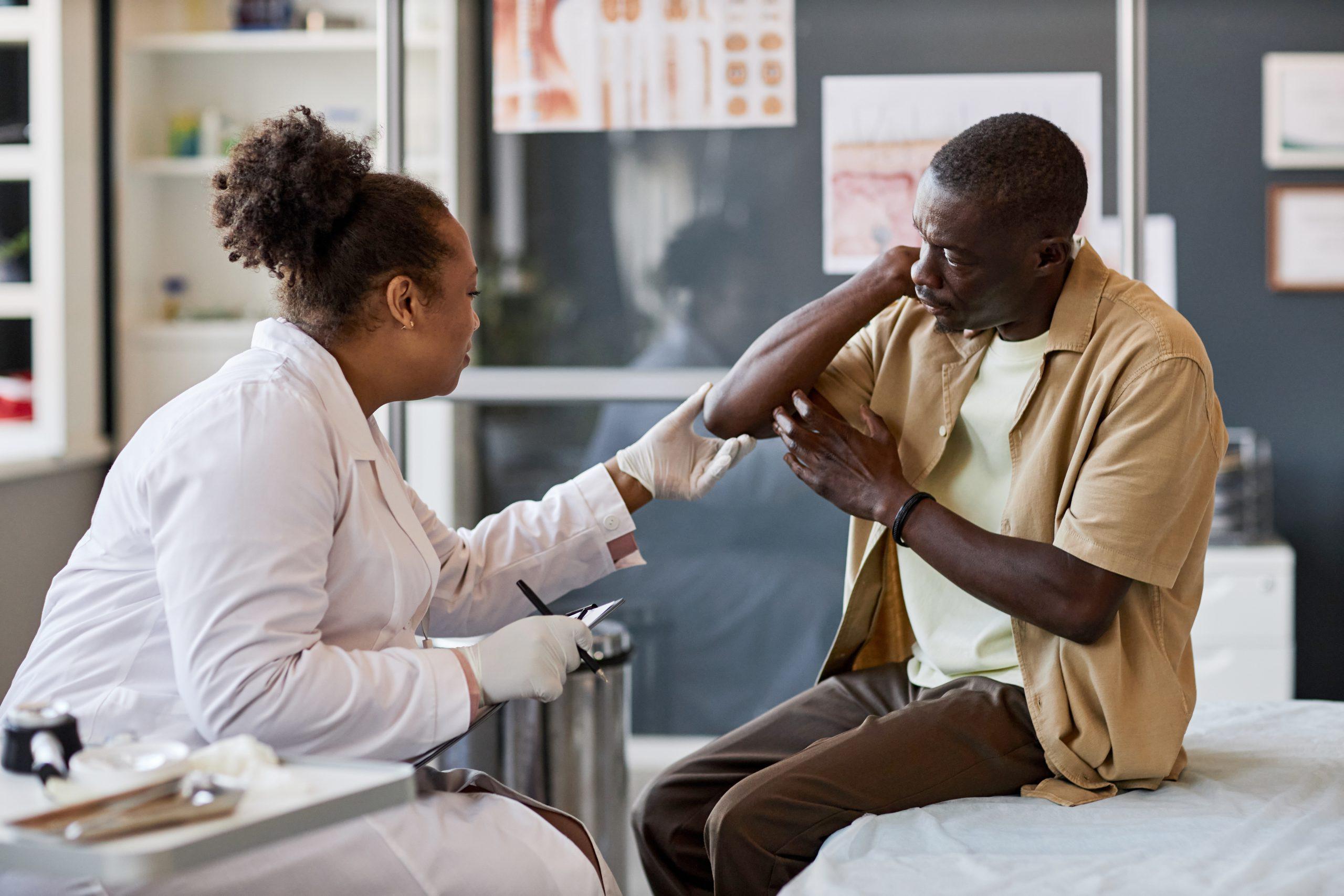 Side view portrait of African American woman as a physician consulting an older male
patient in a clinic and examining skin