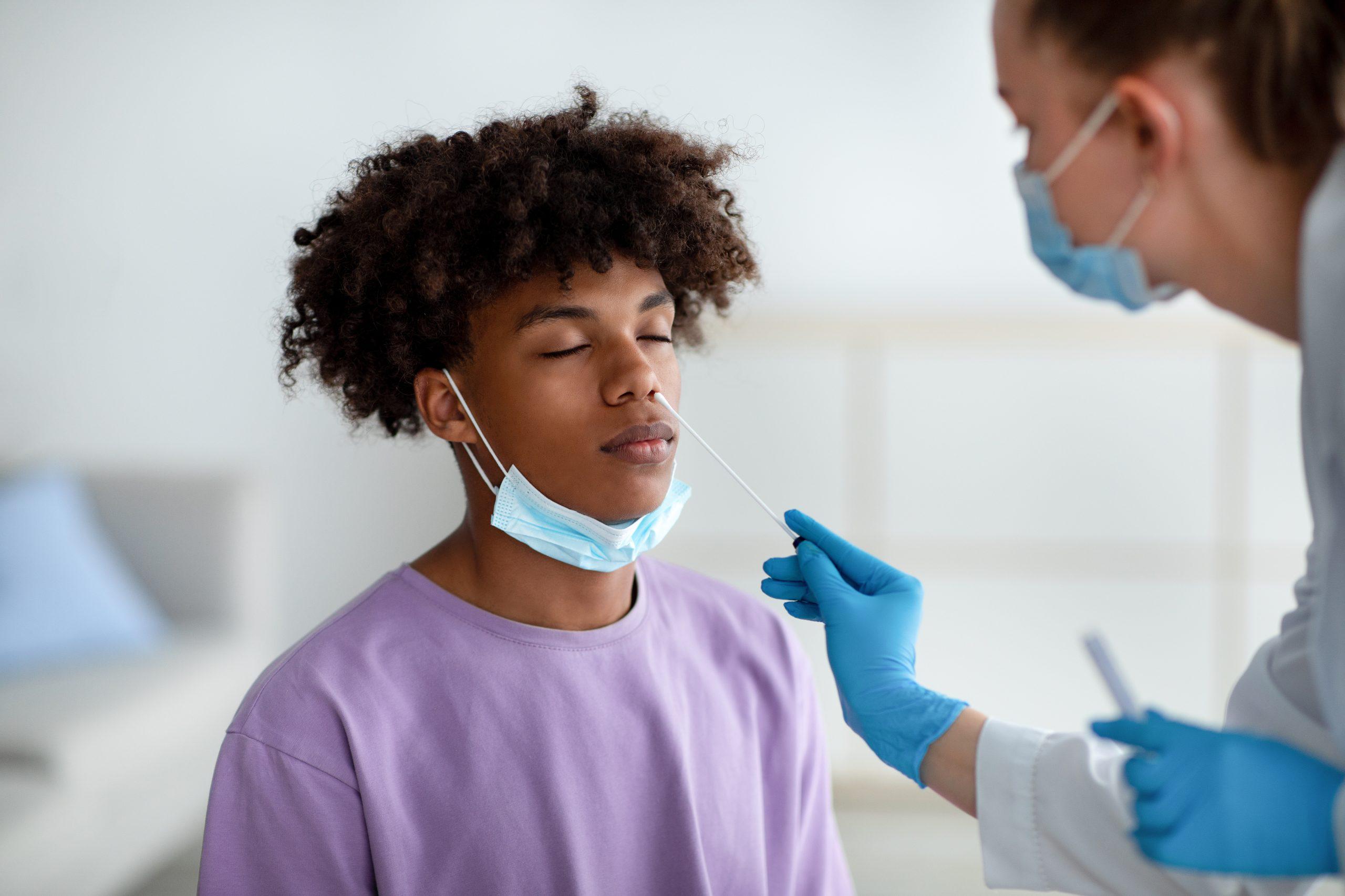 Female doctor conducting a coronavirus PCR test for black teenager at a clinic.