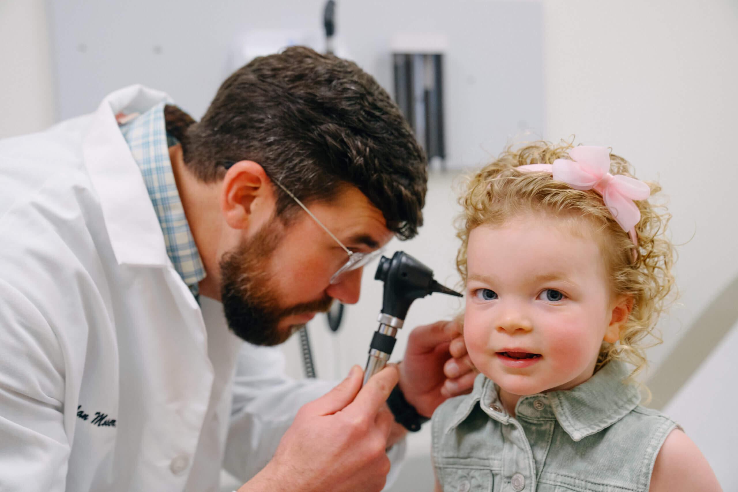 Young girl has her ears checked by a healthcare provider.