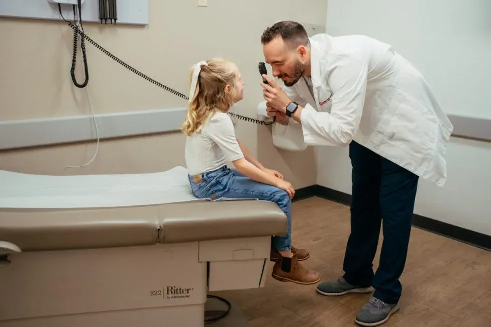 Male doctor checking a girl's eyes with his Otoscope