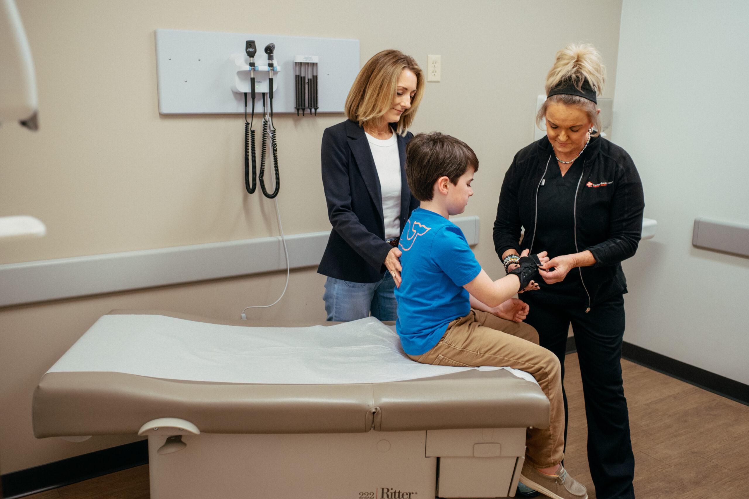 Pediatric healthcare professional examining and treating a young patient's wrist during a medical appointment.