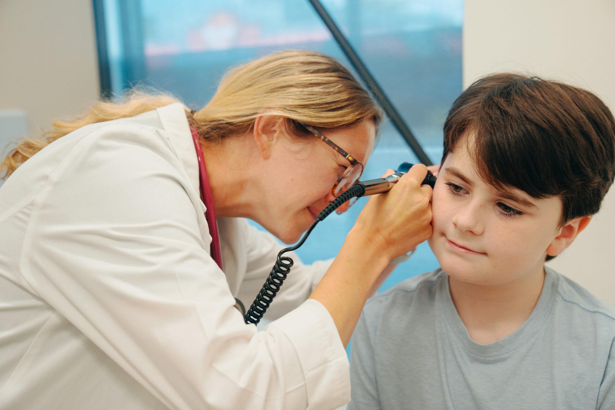 Pediatric patient undergoing swimmer's ear and ear infection evaluation as an AFC healthcare provider uses an otoscope to examine his right ear during a pediatric urgent care visit. 