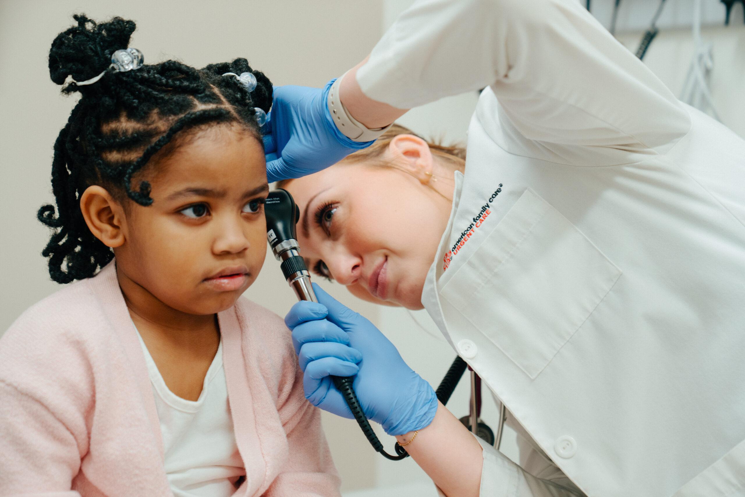 Pediatric patient undergoing swimmer's ear and ear infection evaluation as an AFC healthcare provider uses an otoscope to examine her left ear during an urgent care visit. 