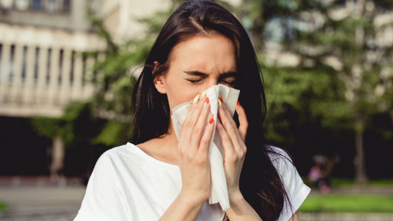 Woman outside and blowing her nose into a tissue due to allergies