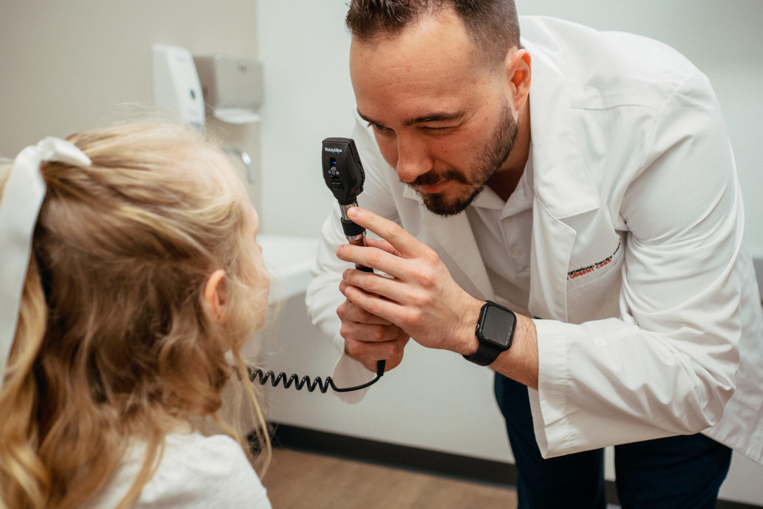 Young girl sitting comfortably on an exam table while an AFC medical provider checks her eyes during a pediatric urgent care visit.