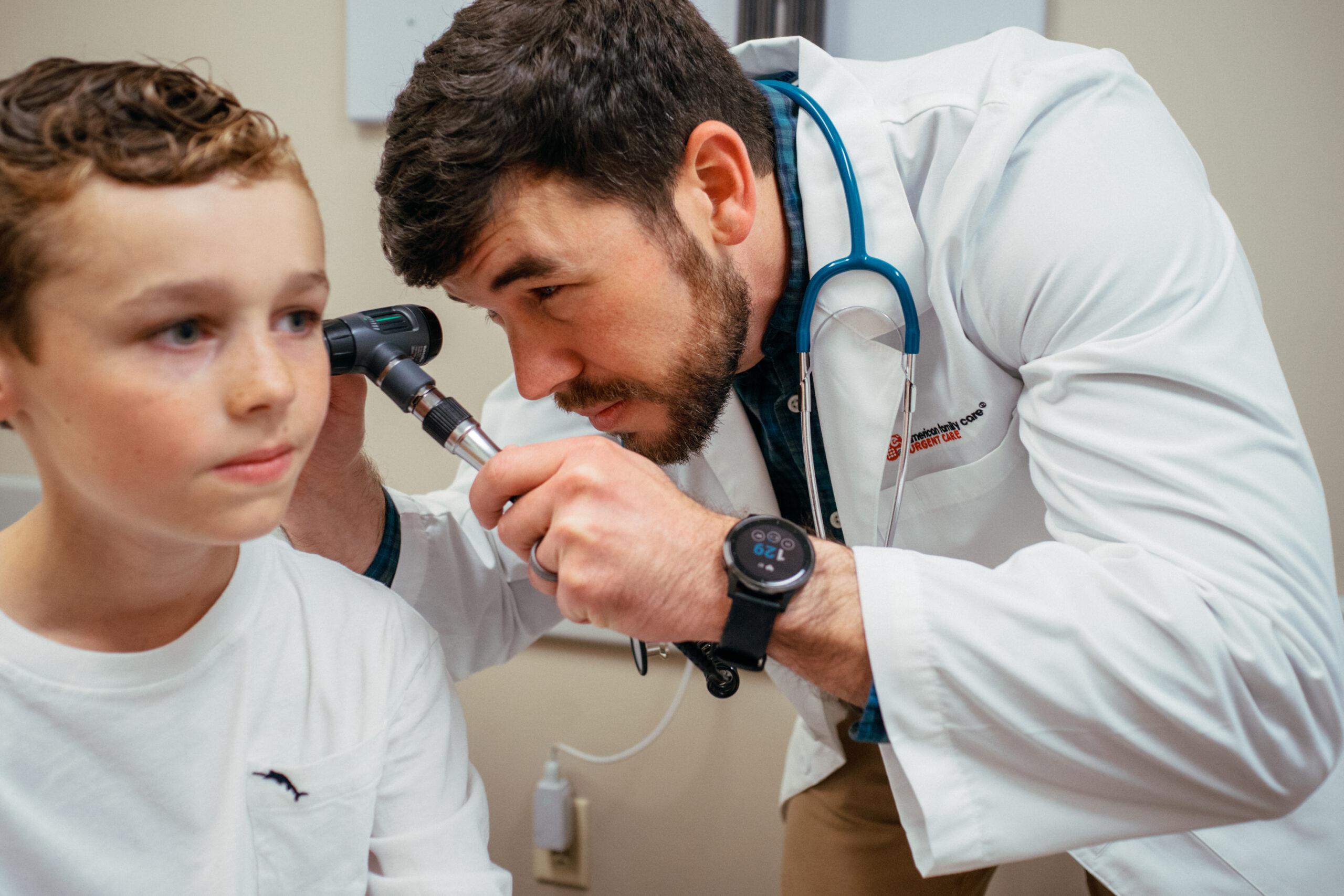 Pediatric male patient having his left ear checked by an AFC healthcare provider for symptoms of swimmer&rsquo;s ear.
