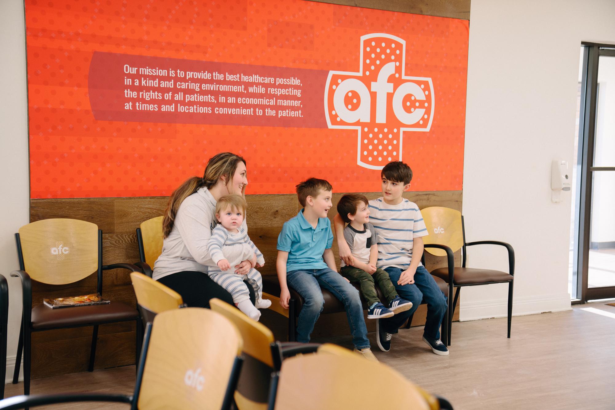 A smiling family sits in the waiting room of an AFC Urgent Care.