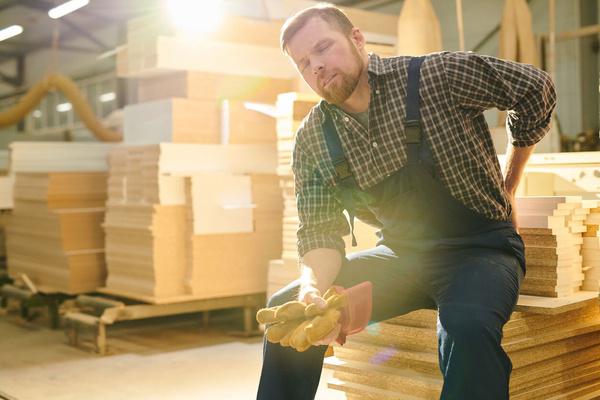 Worker sitting on stacked lumber holding his injured knee