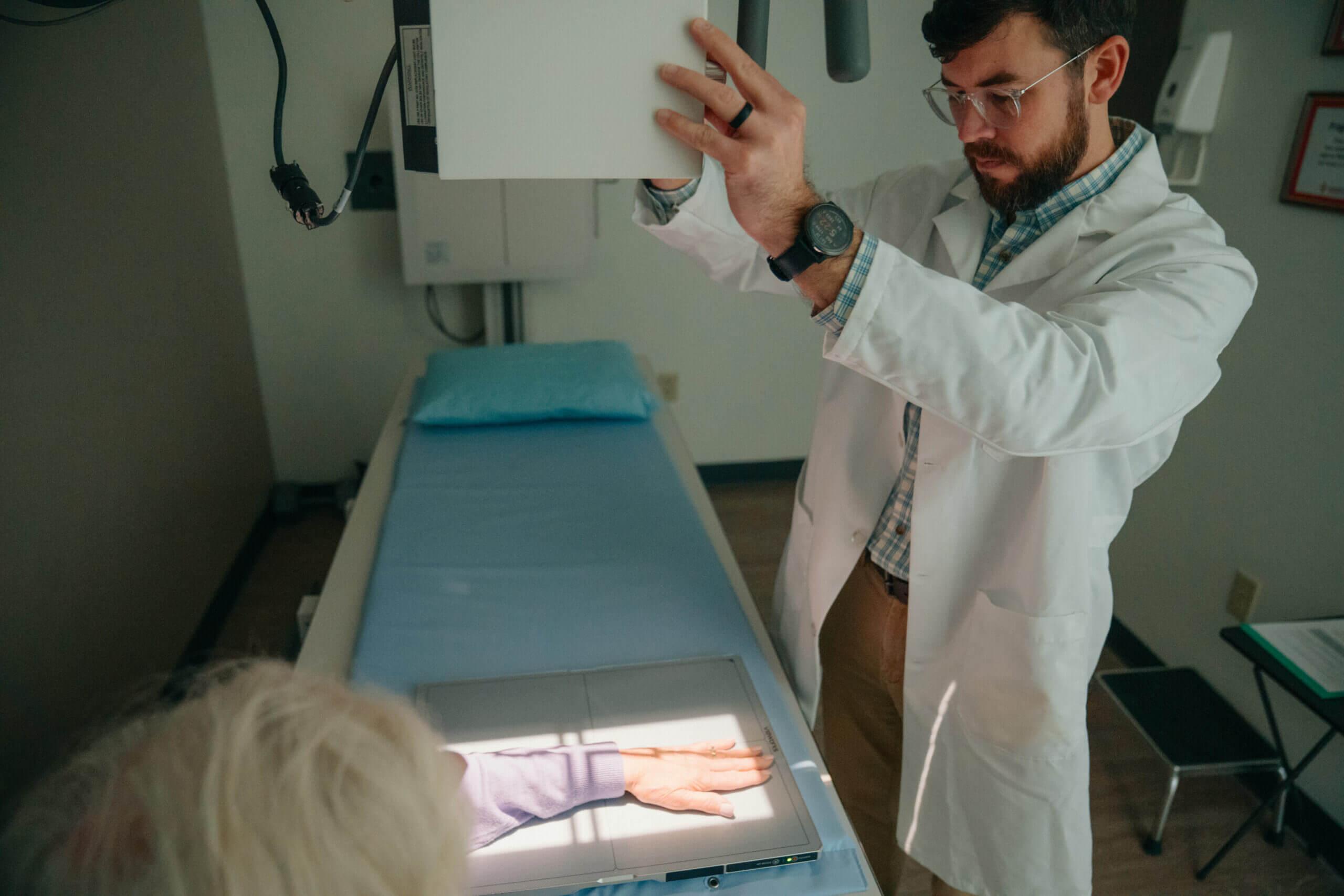 A female patient having her left arm x-rayed by a male AFC healthcare provider. The provider is placing x-ray machine above her left wrist for imaging.