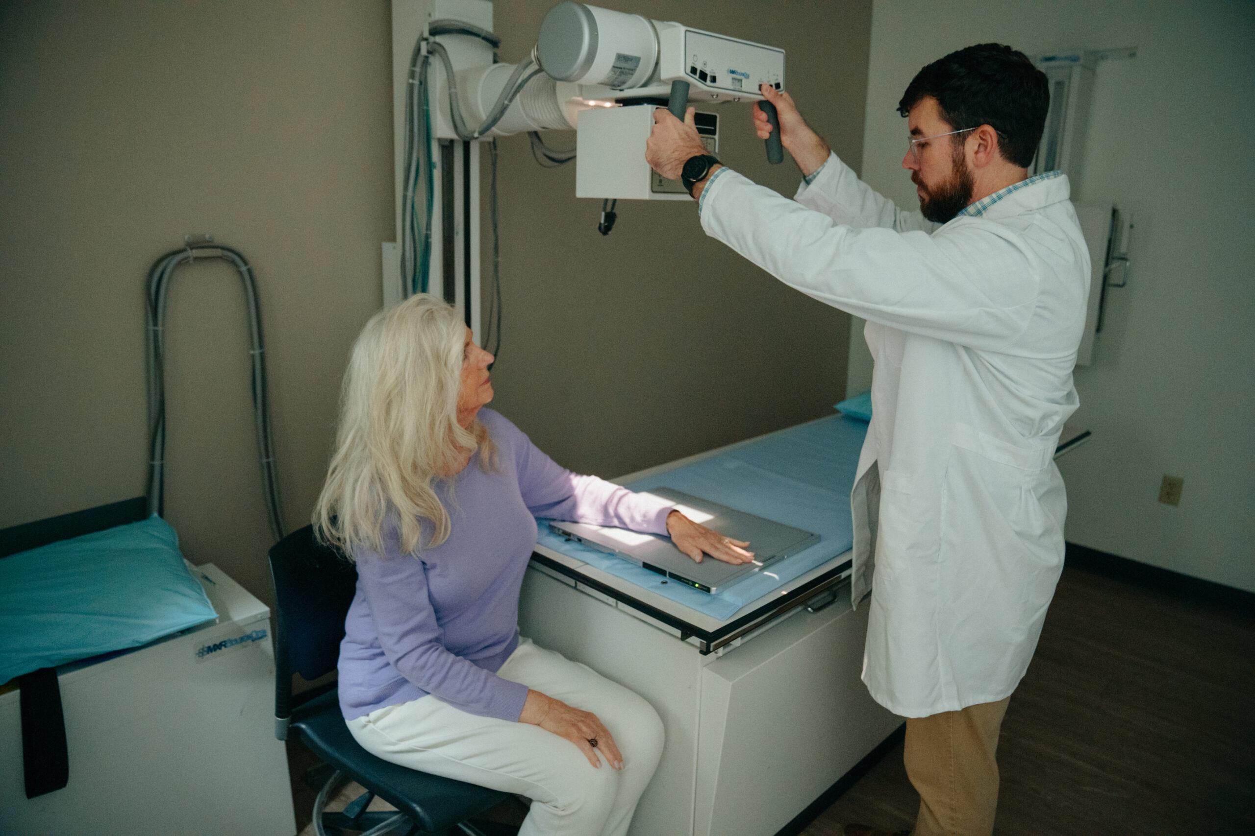 A female patient having her left arm x-rayed by an AFC healthcare provider. The patient is seated comfortably in a clean, modern imaging room.